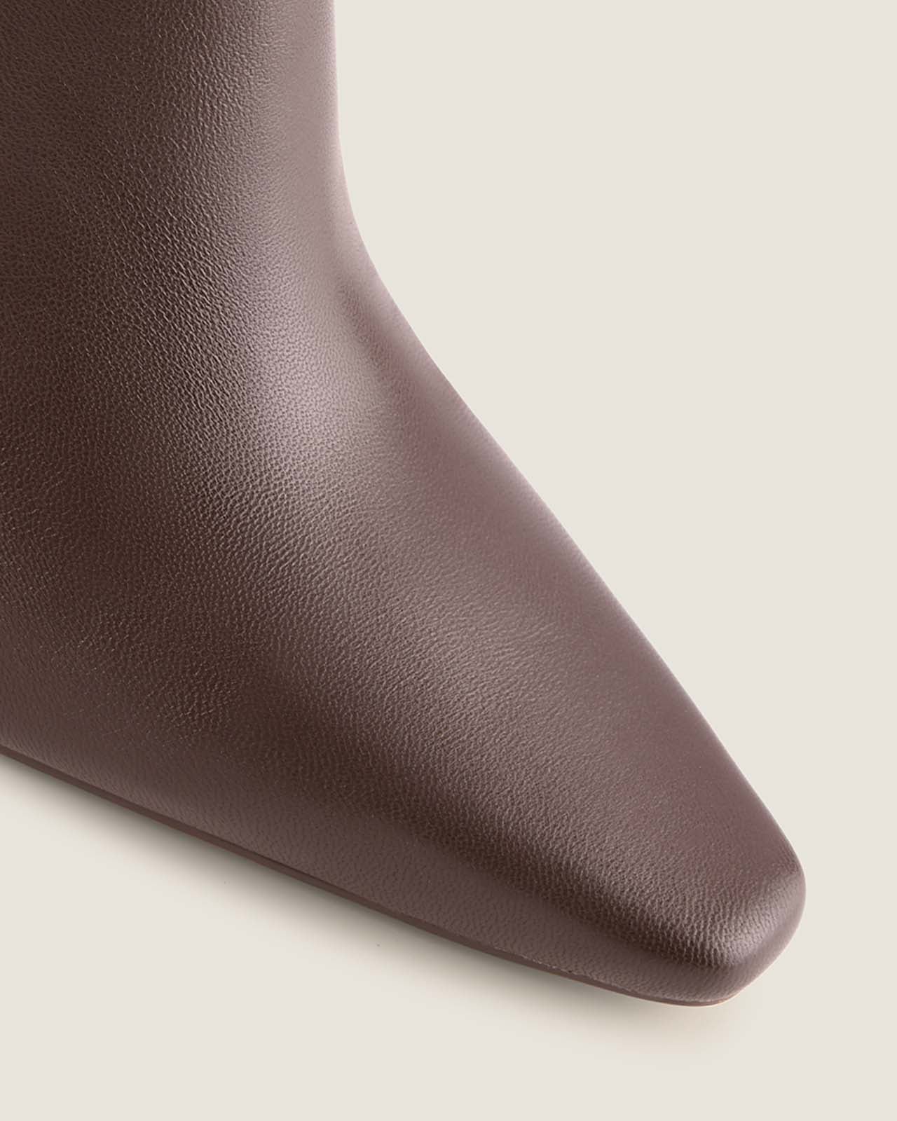Close-up of a brown leather boot with a pointed toe on a light beige background
