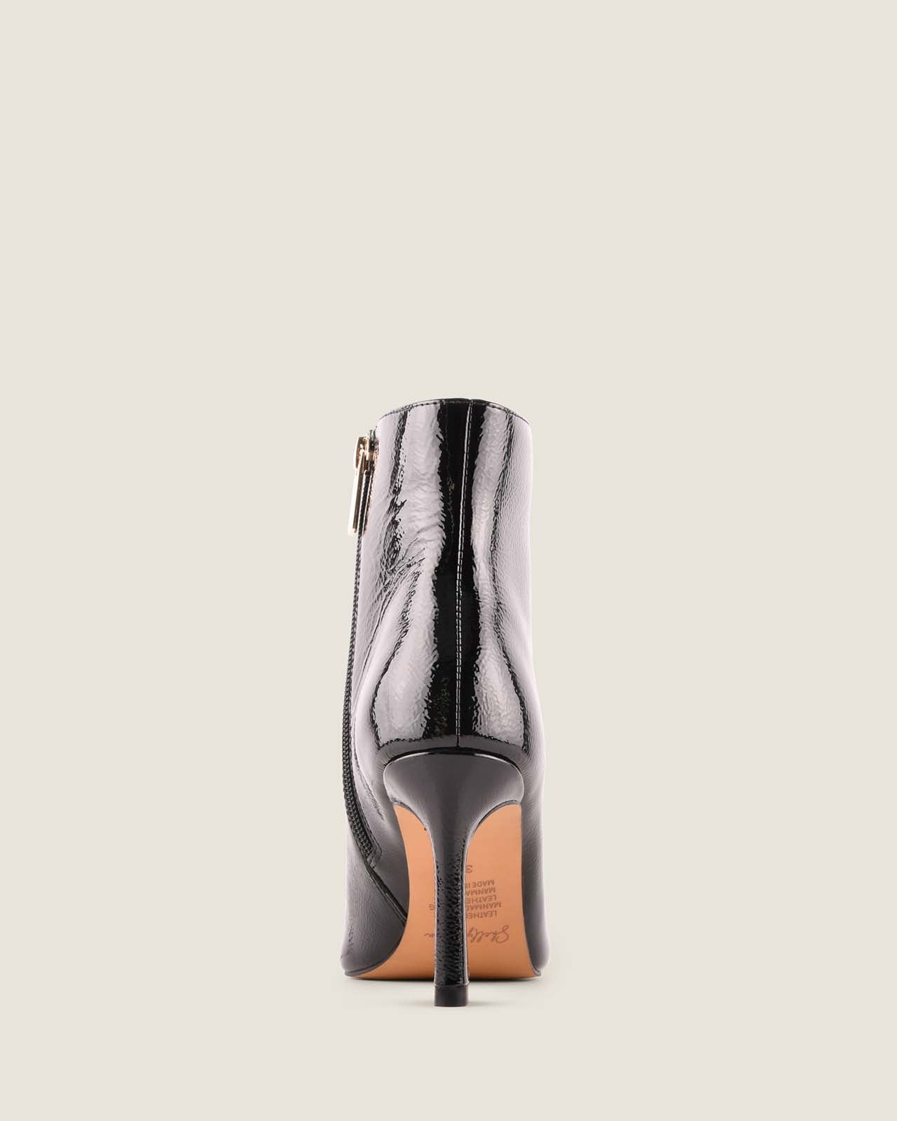 Black patent leather ankle boot on a light beige background
