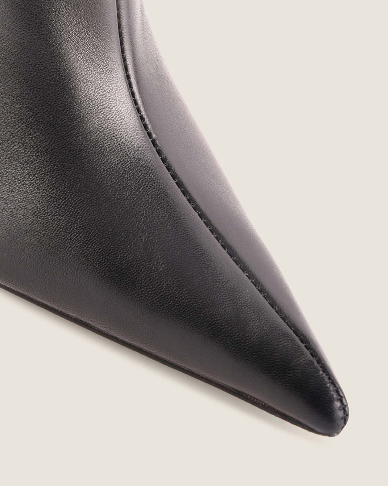 Close-up of a black leather shoe with a pointed toe on a light background