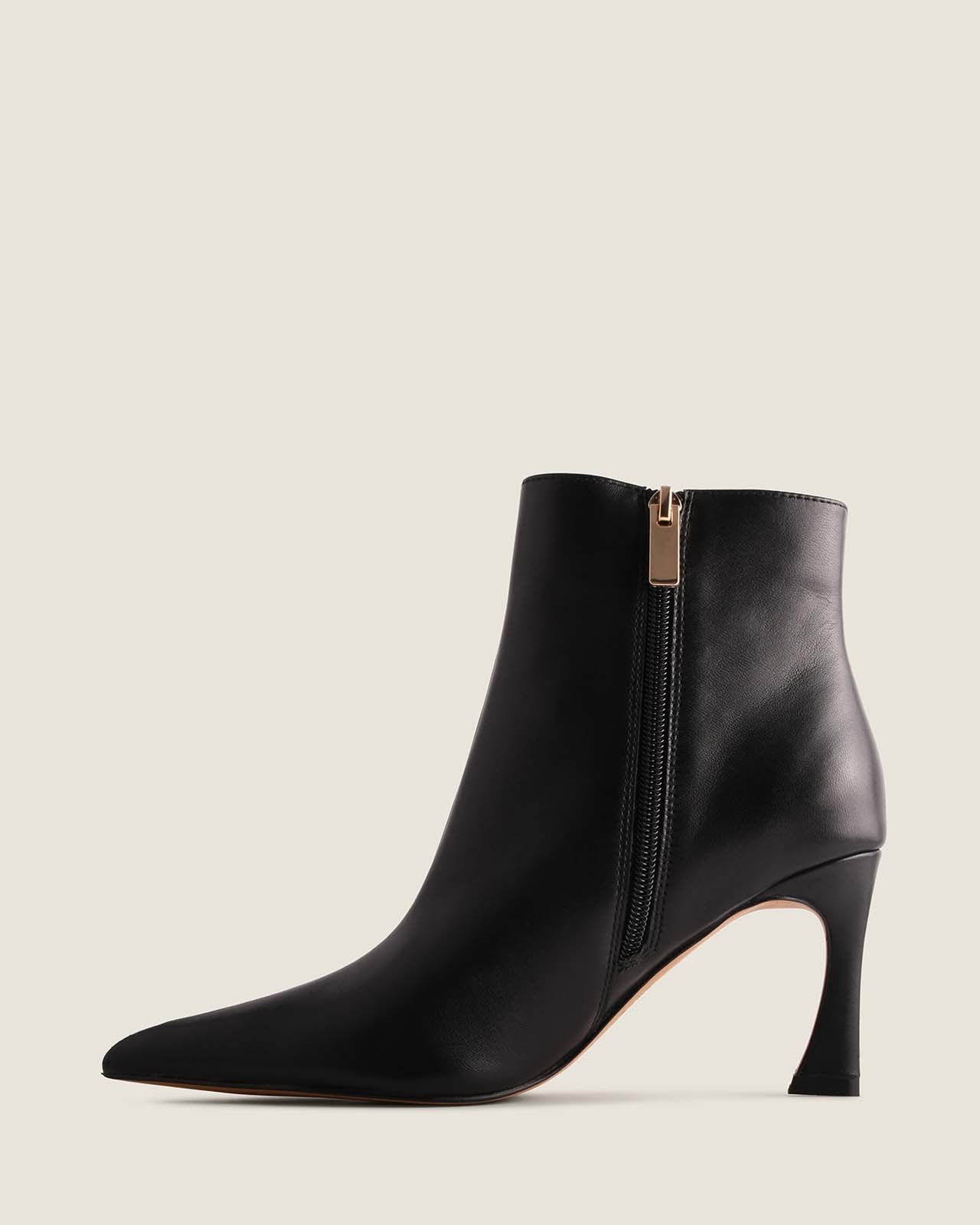 Black ankle boot with a gold zipper on a light grey background