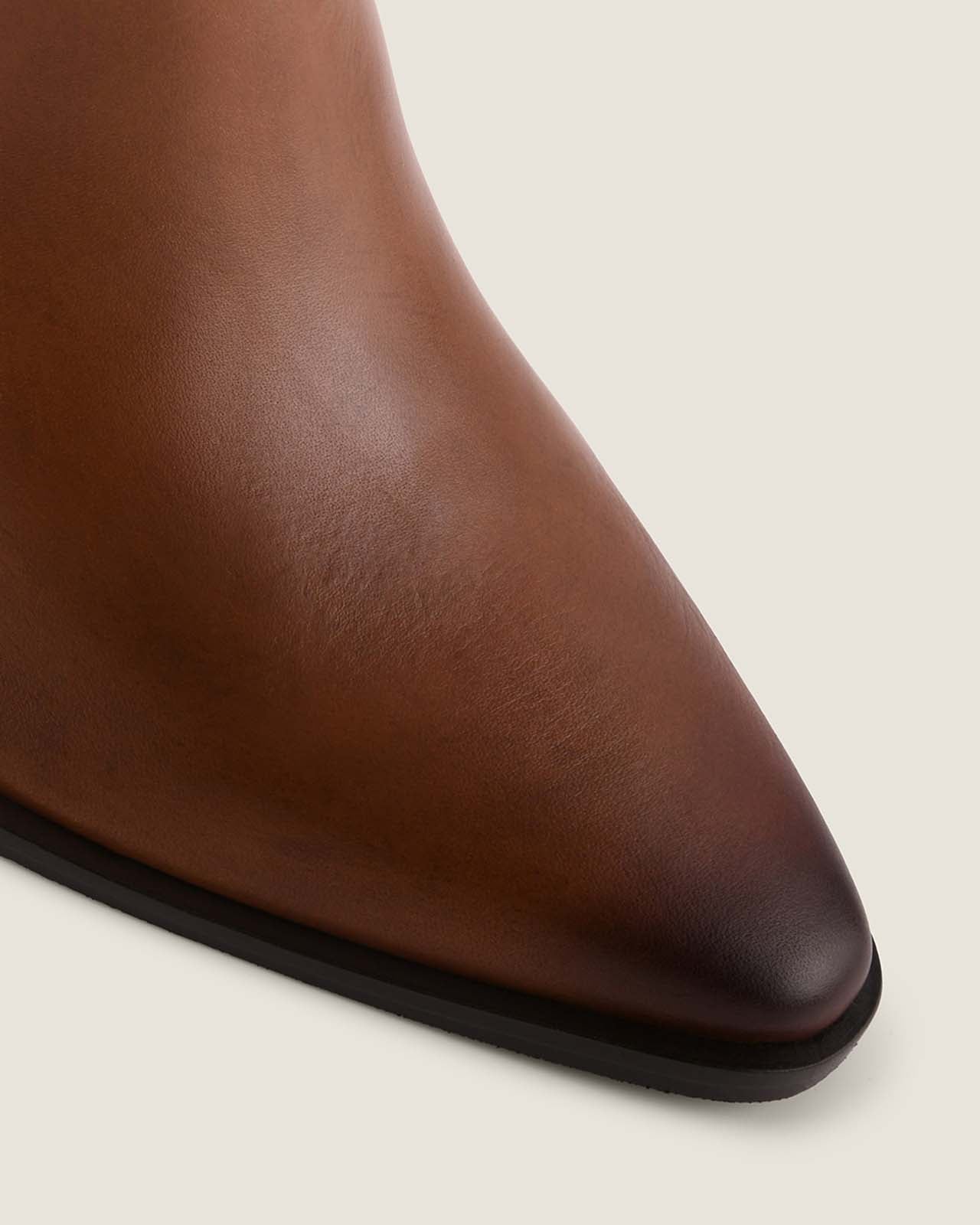 Close-up of a brown leather ankle boot with a pointed toe on a light beige background