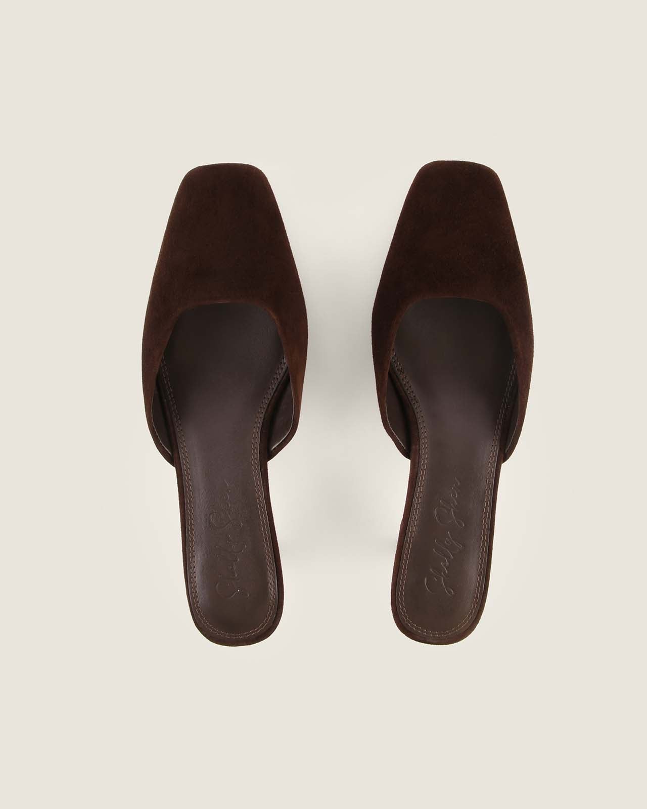 Pair of brown suede mules on a light beige background