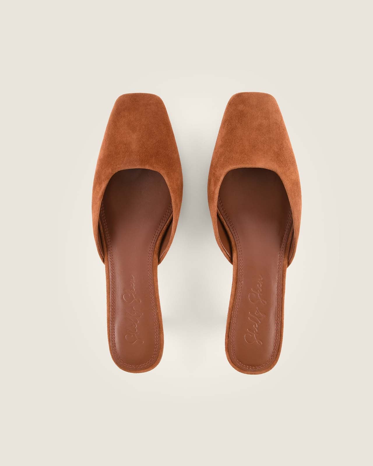 Pair of tan suede mules on a light beige background