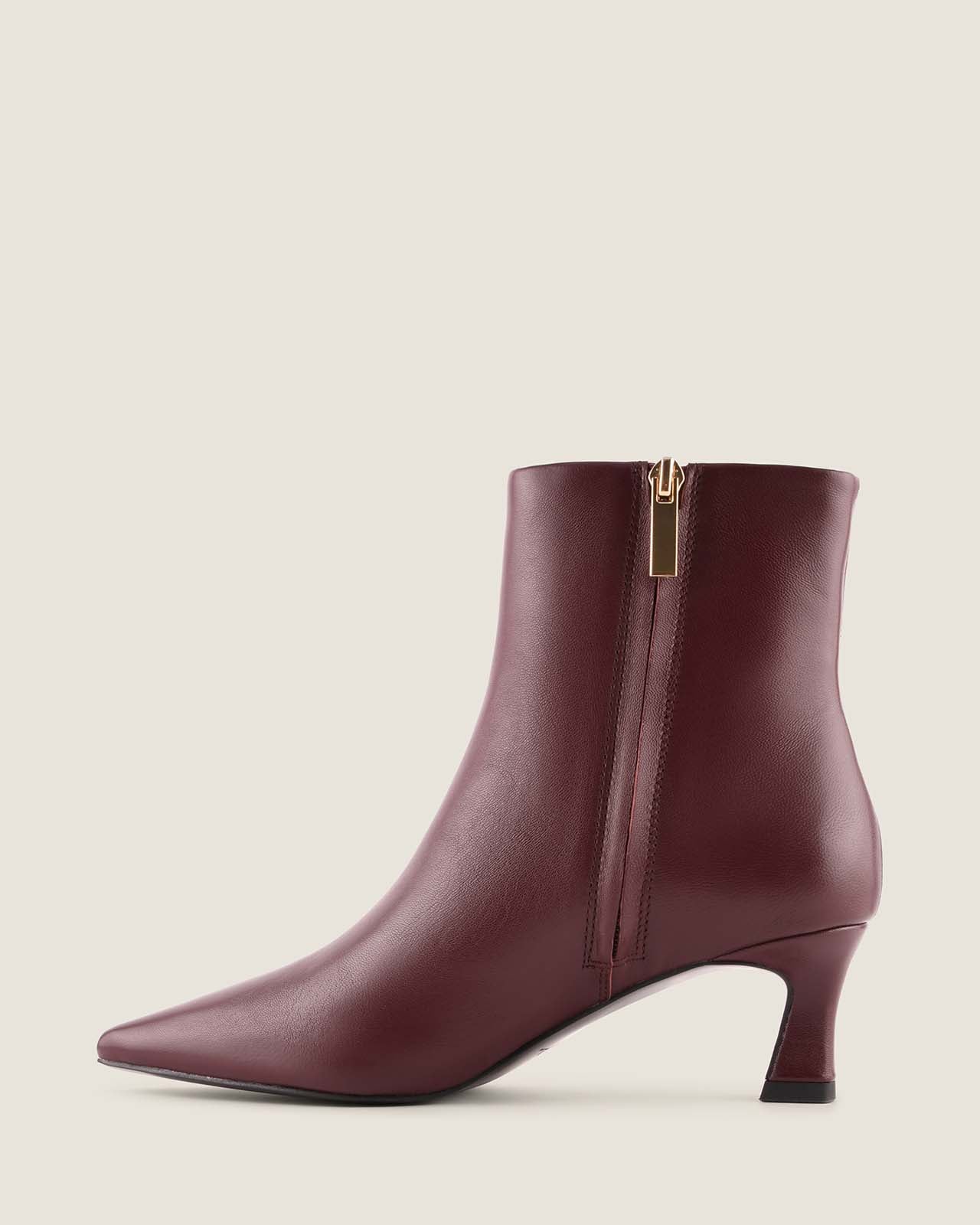 Burgundy ankle boot with a gold zipper on a light beige background