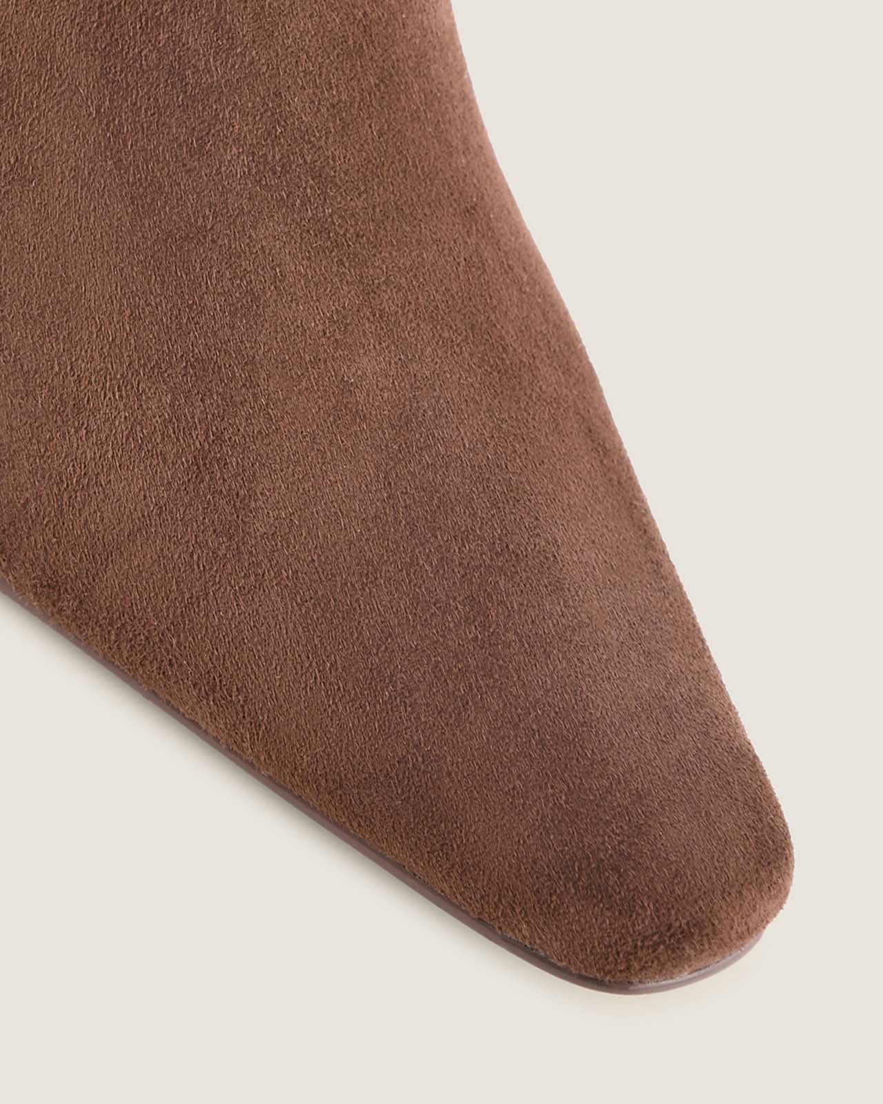 Close-up of a chocolate suede shoe with a pointed-toe on a light beige background