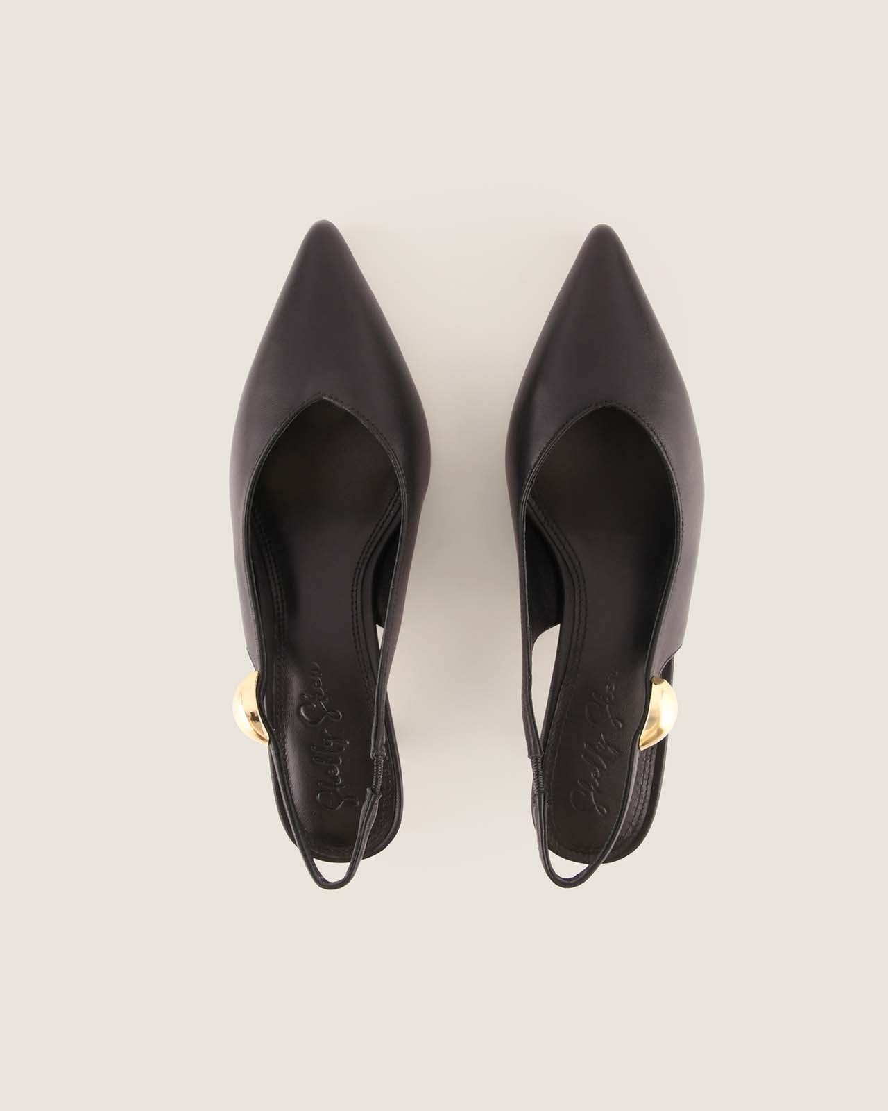 Pair of black slingback heels with a gold ornament detail on a light beige background