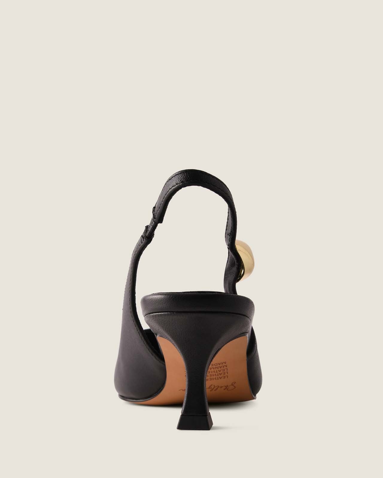 Black slingback heel with a gold ornament detail on a light beige background