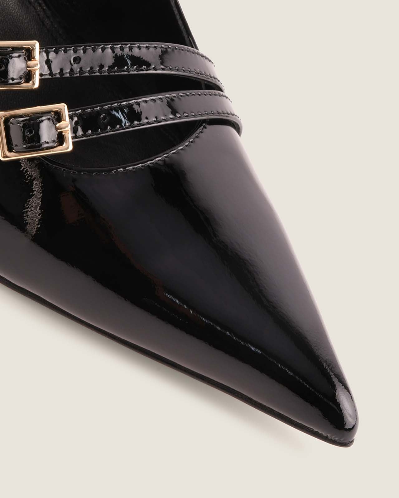 Black patent leather pointed-toe shoe with gold buckles on a light background