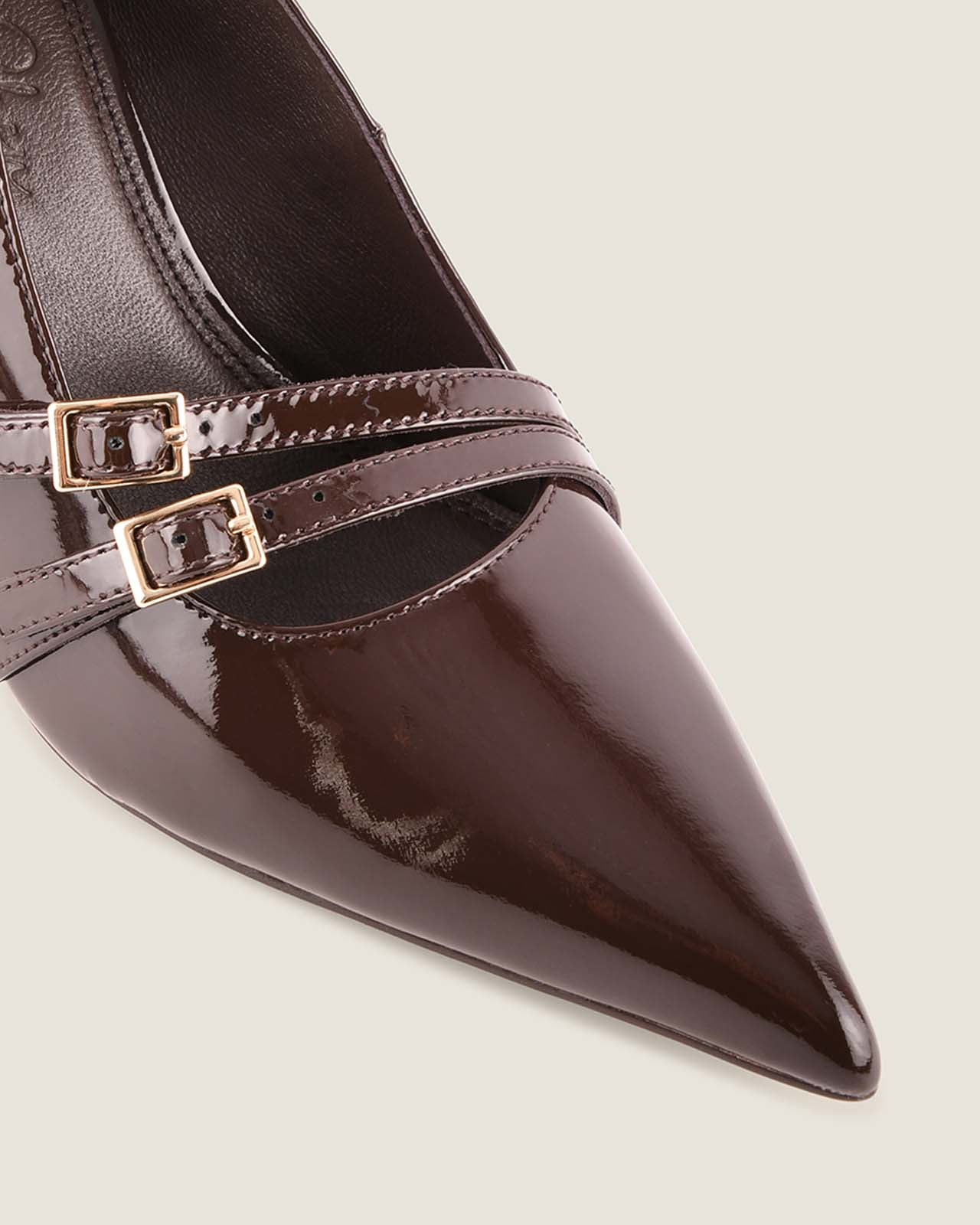 Brown patent leather shoe with gold buckles on a light background