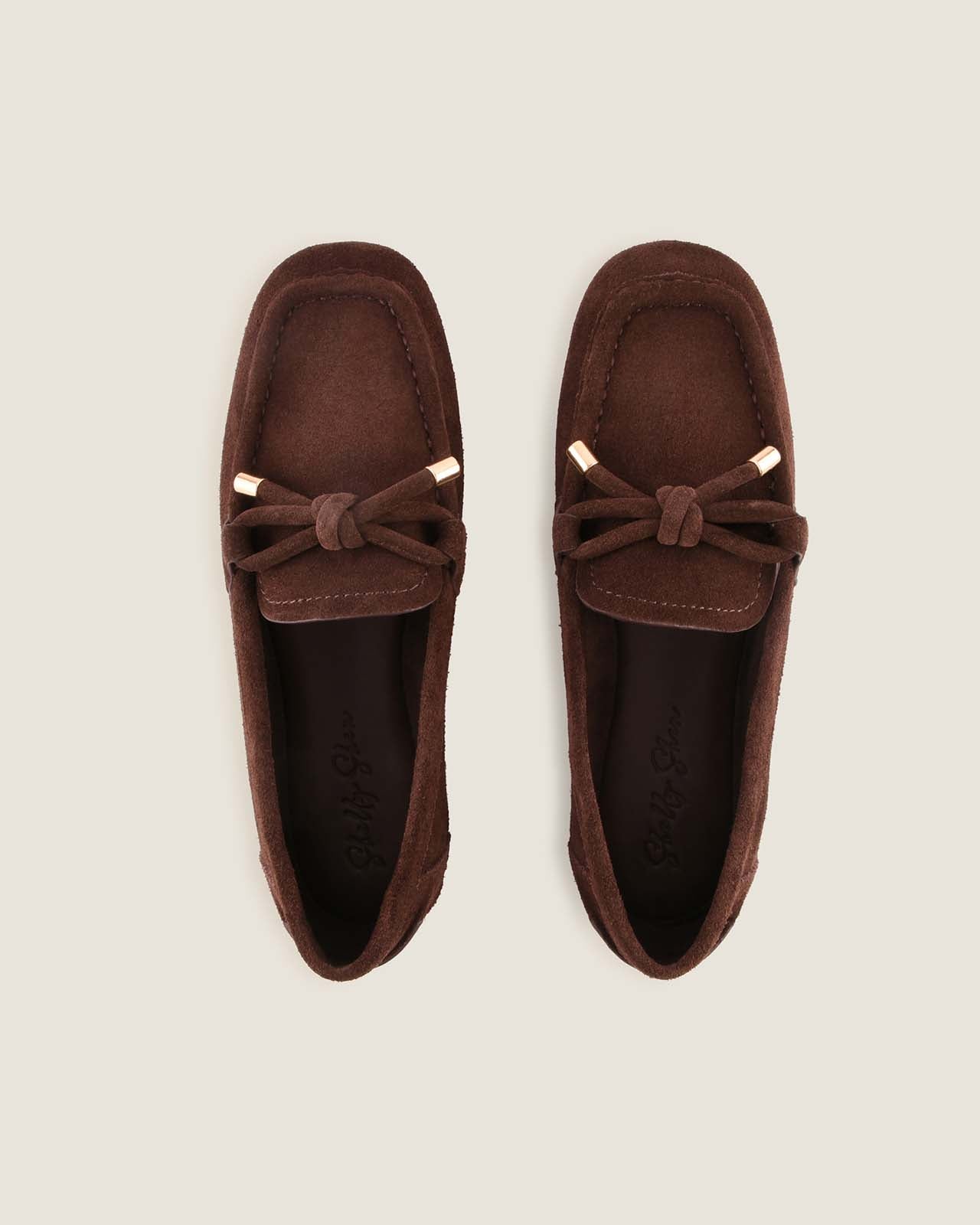 Pair of brown suede loafers with a bow on a light grey background
