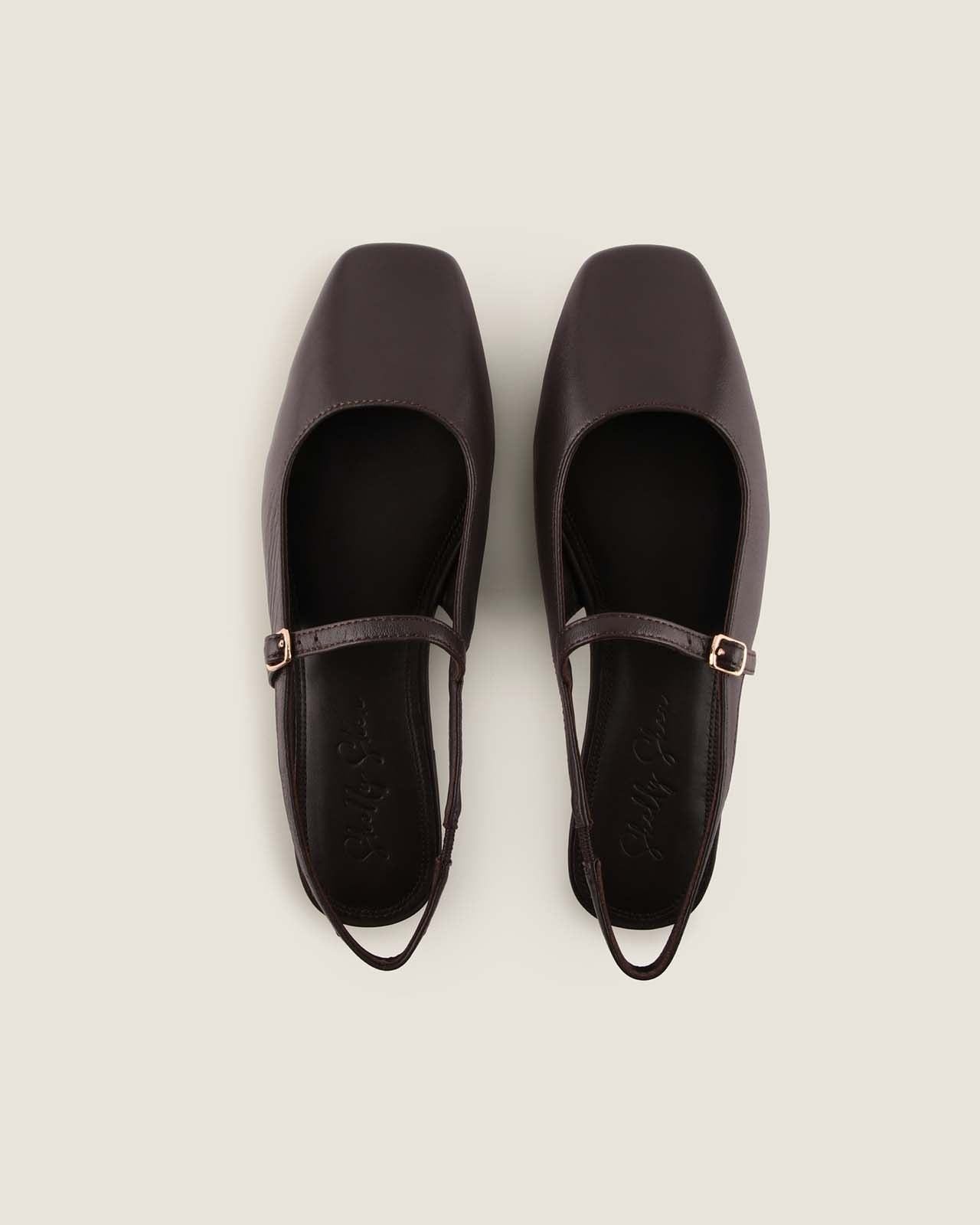 Pair of brown leather shoes with square toes and thin straps on a light grey background