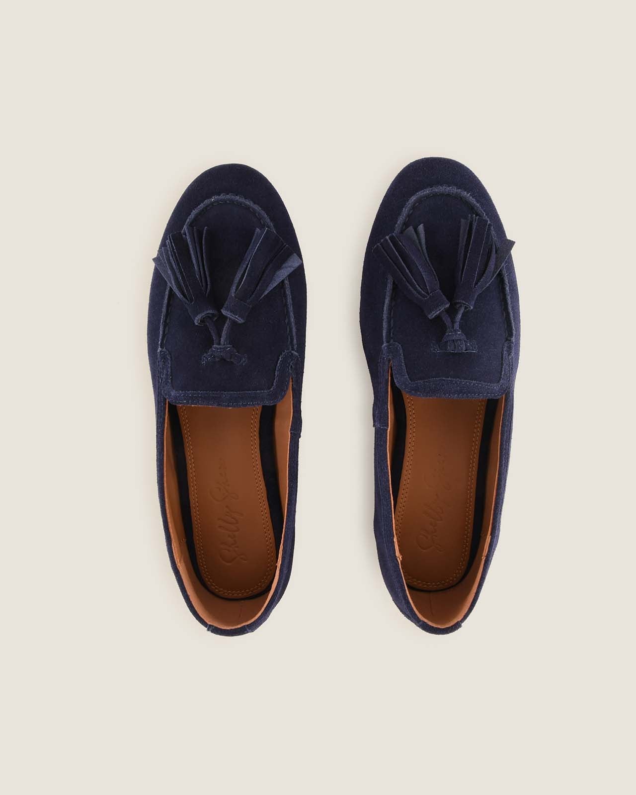 Pair of navy blue loafers with tassels on a beige background