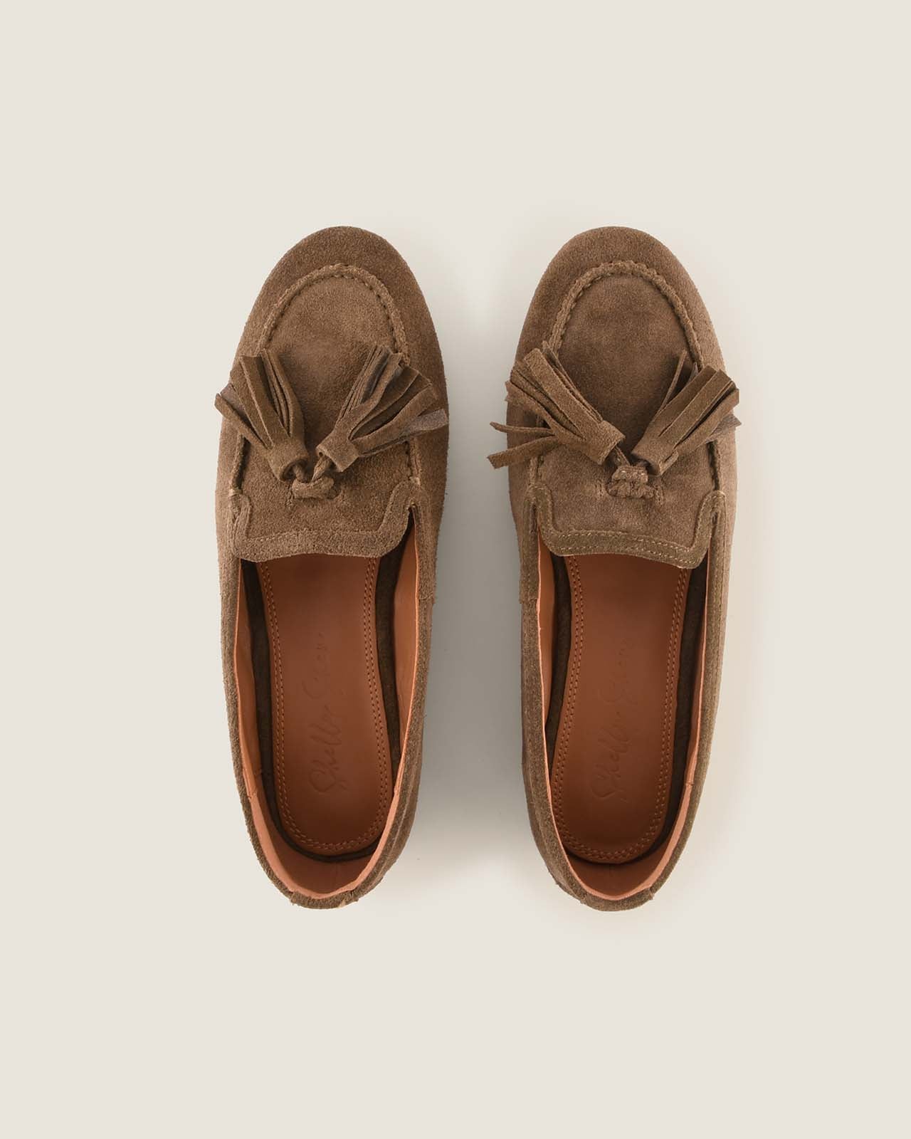 Pair of olive suede loafers with tassels on a light beige background