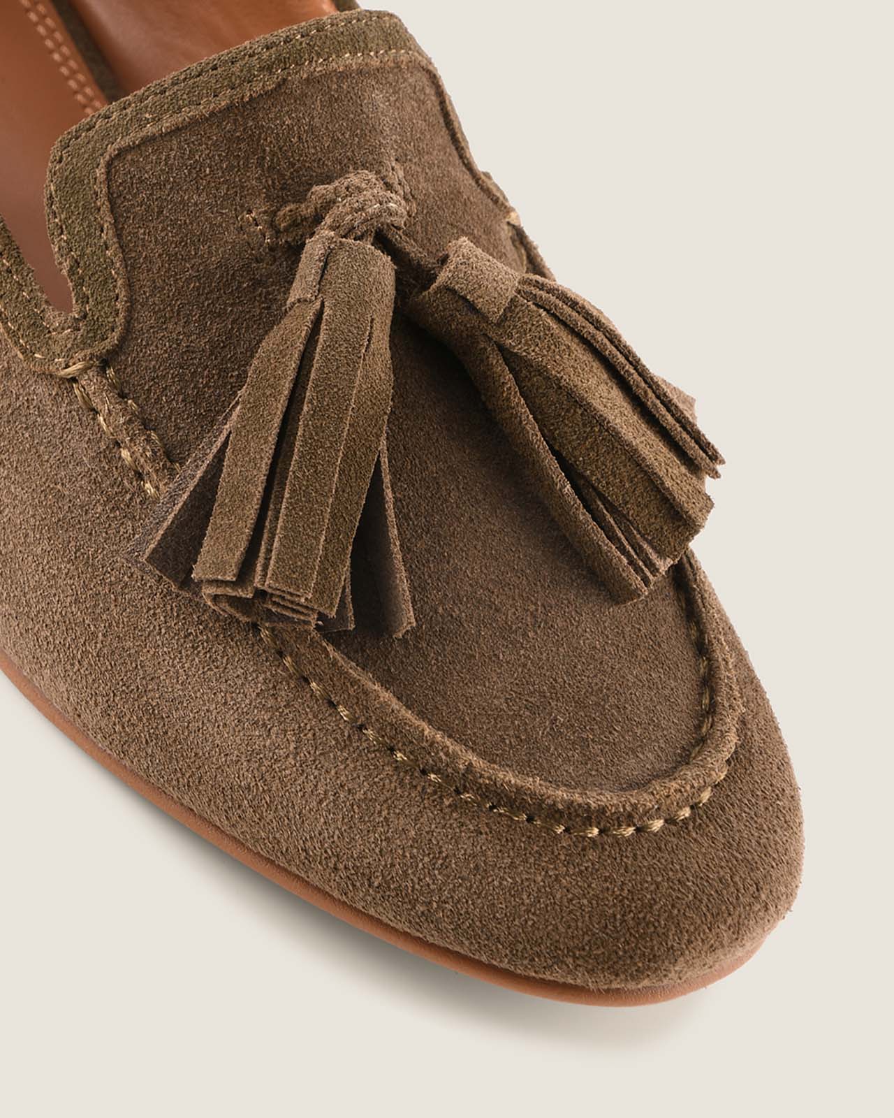 Olive suede loafer with tassels on a light grey background