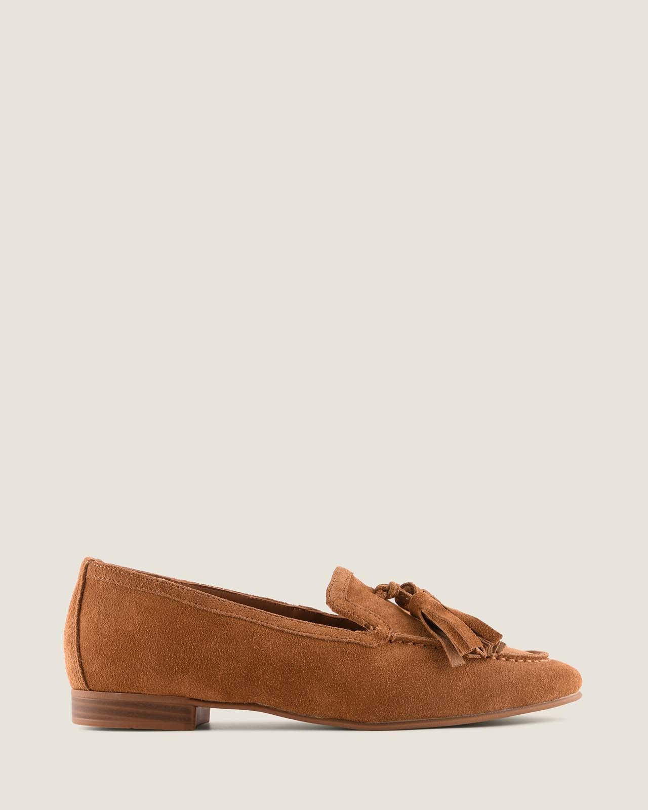 Tan suede loafer with tassel on a light grey background