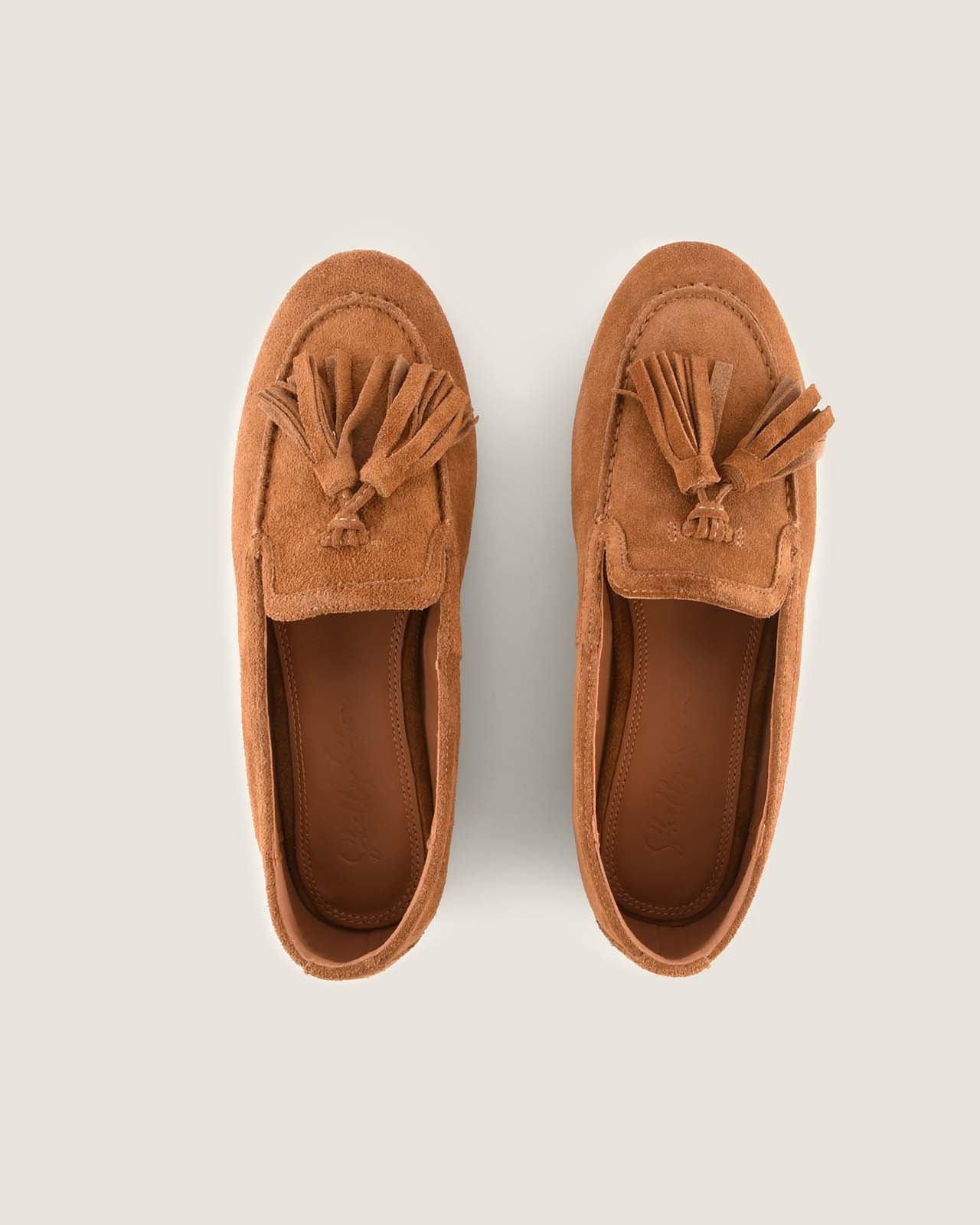 Pair of tan loafers with tassels on a light grey background