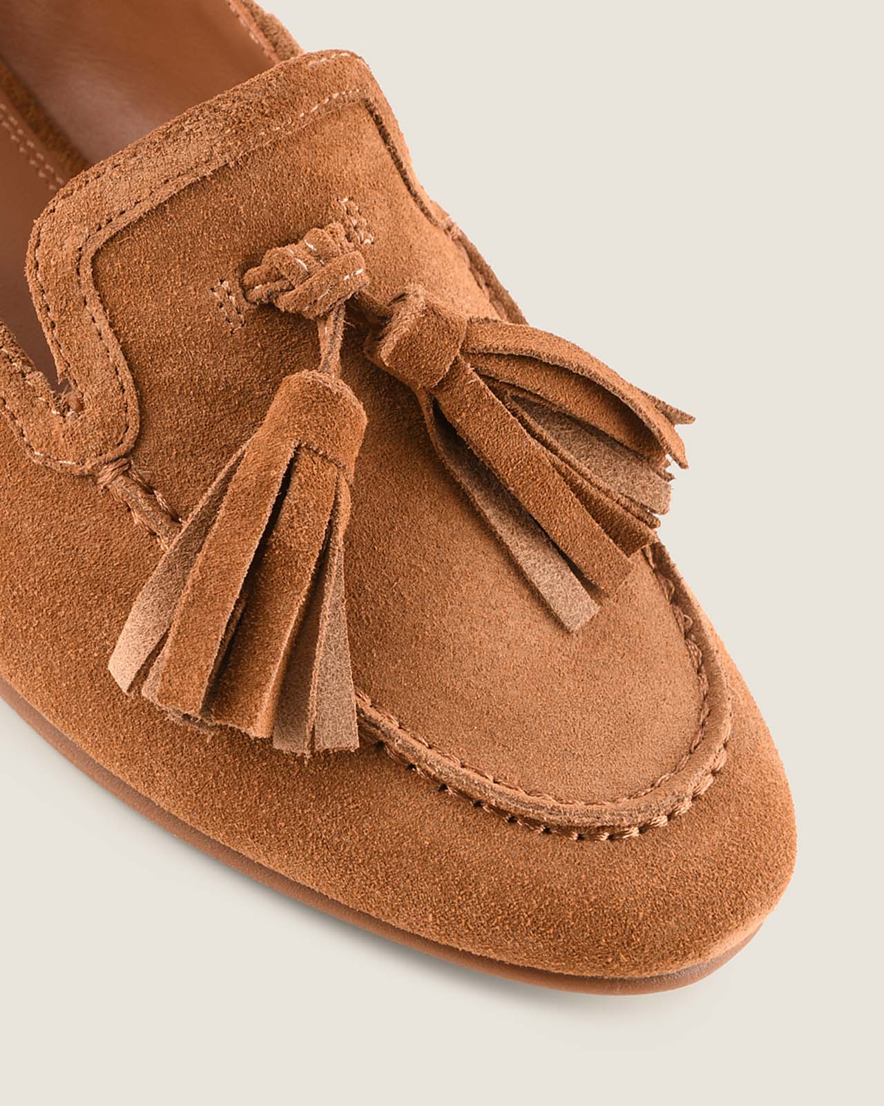 Tan suede loafer with tassel on a light grey background