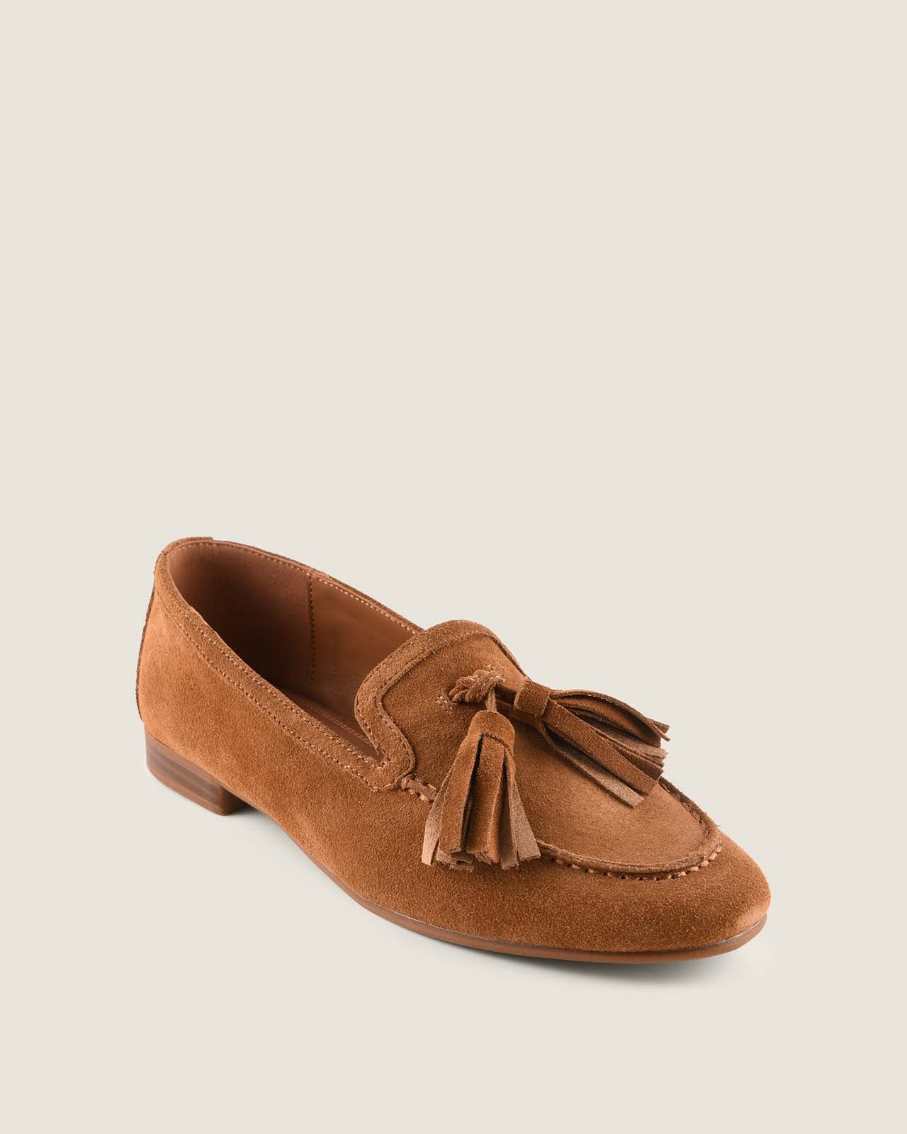 Tan suede loafer with tassel on a light grey background