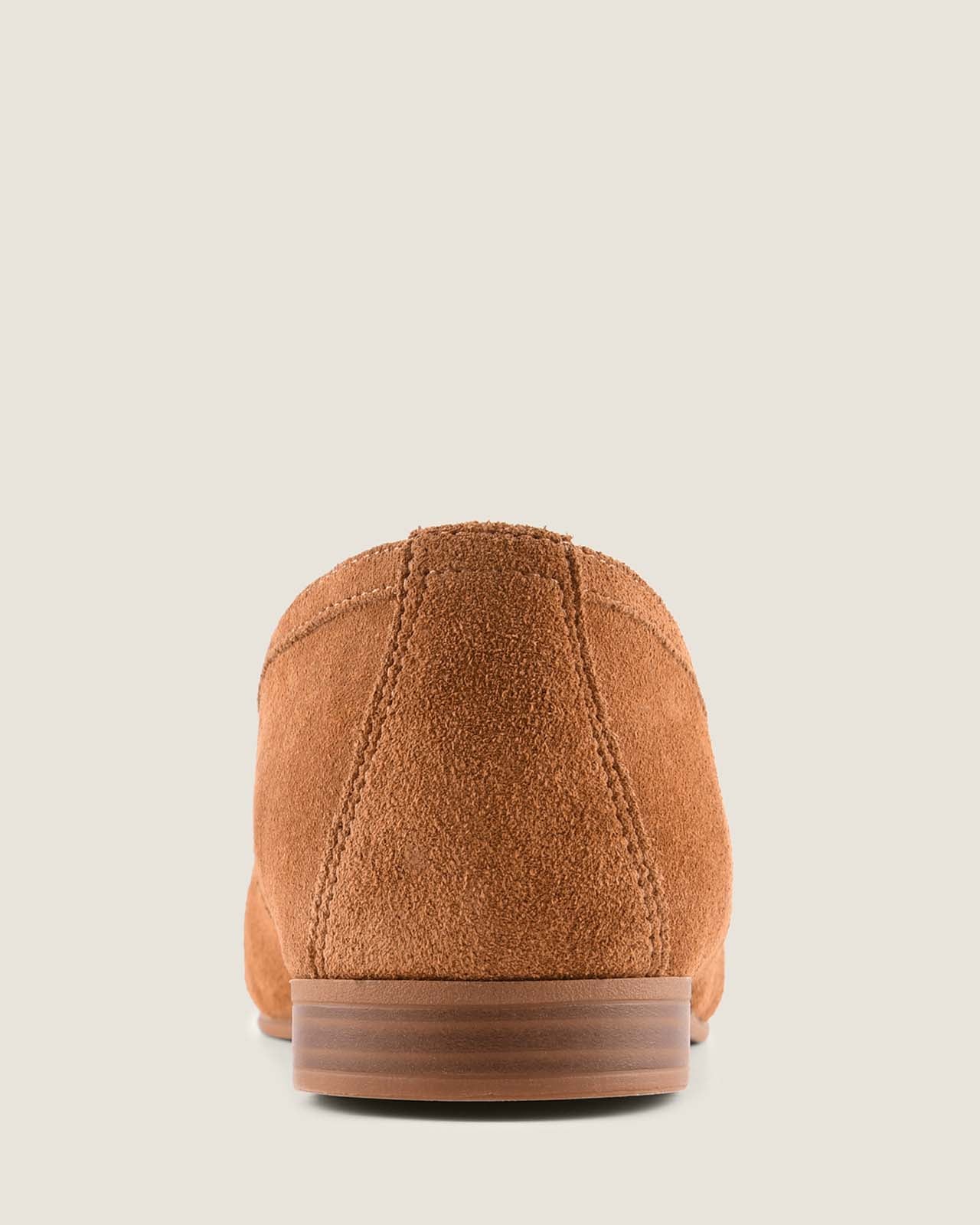 Tan suede loafer with tassel on a light grey background