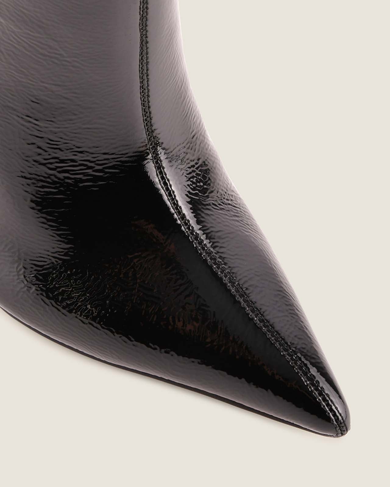 Close-up of a black patent leather pointed-toe boot on a light background