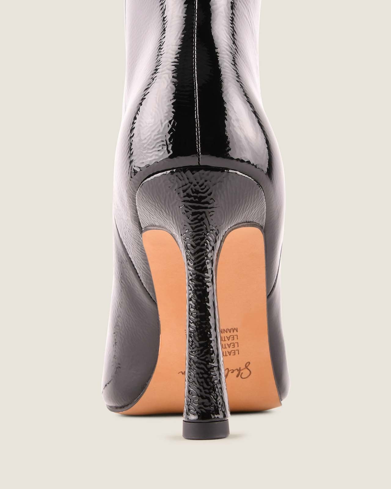 Black high-heeled shoe with a textured sole on a light gray background