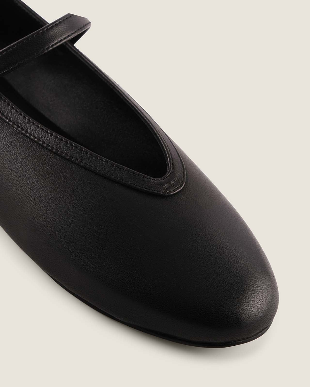 Black flat shoe with a strap on a light gray background