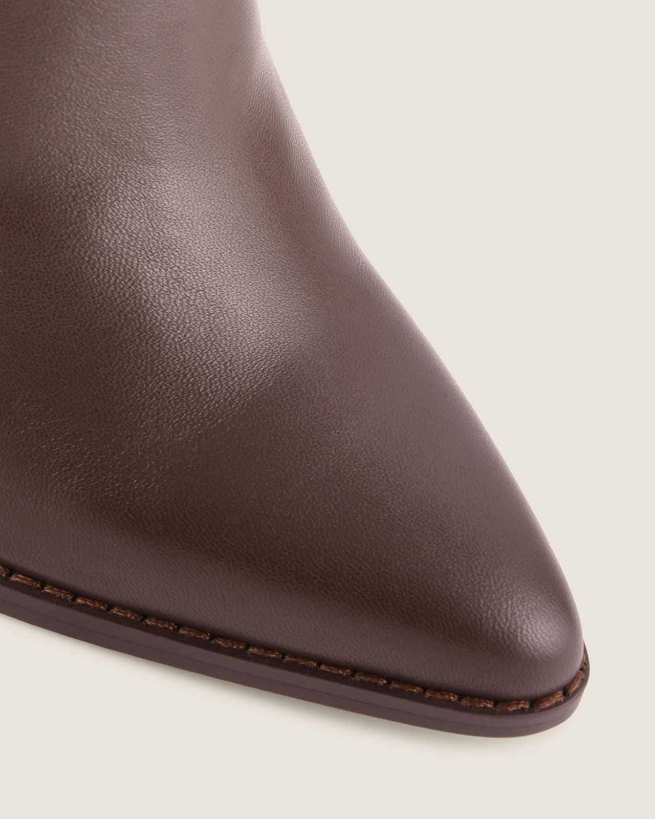 Close-up of a brown leather ankle boot on a light beige background