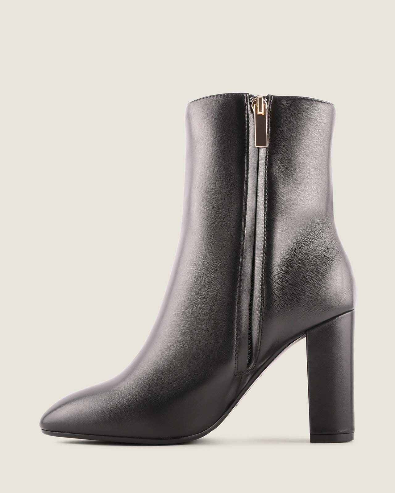 Black ankle boot with a gold zipper on a light gray background