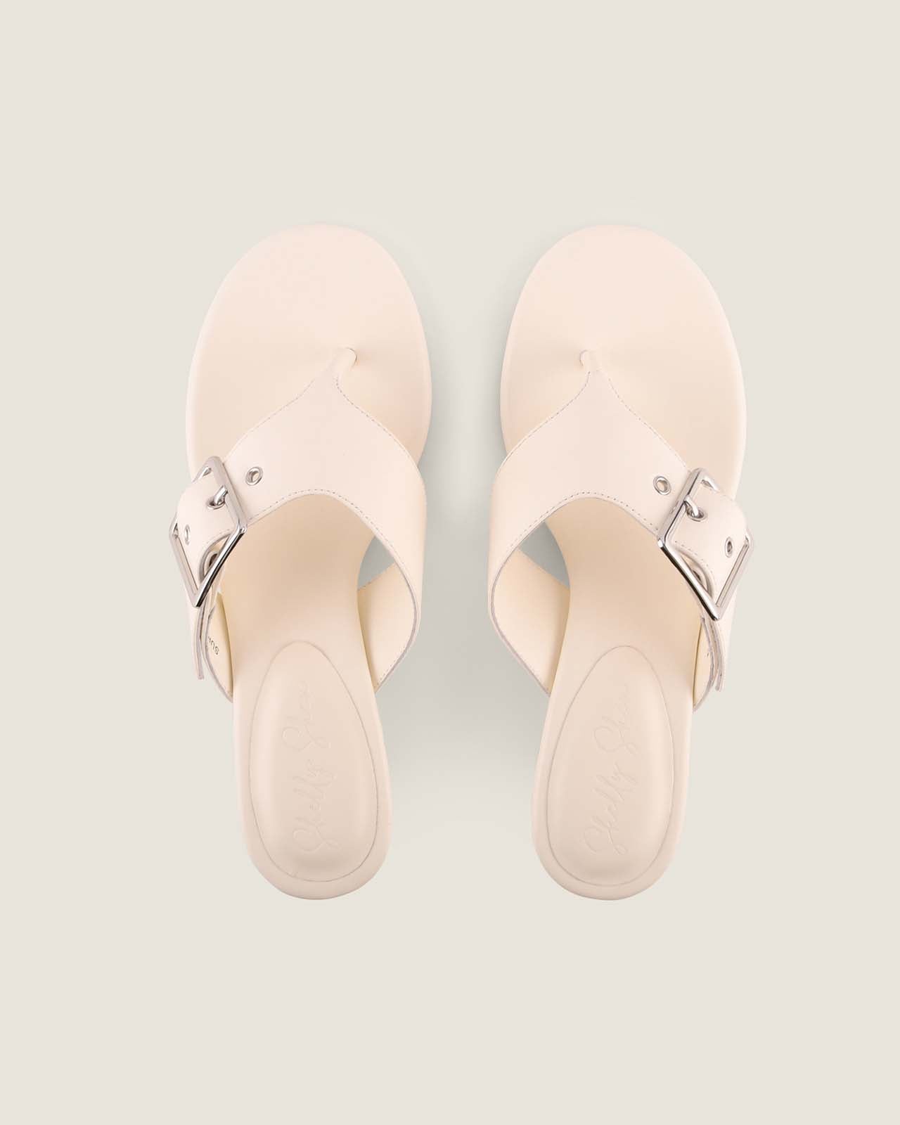 Pair of beige sandals with metallic straps on a light gray background