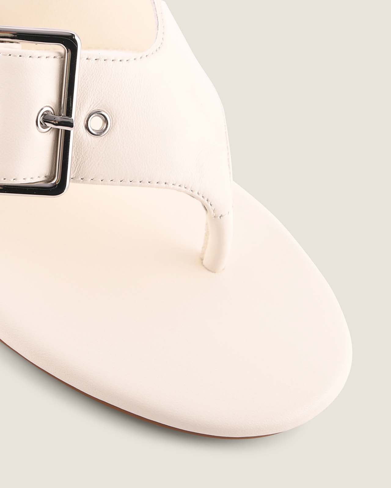 White flat shoe with a buckle on a light gray background