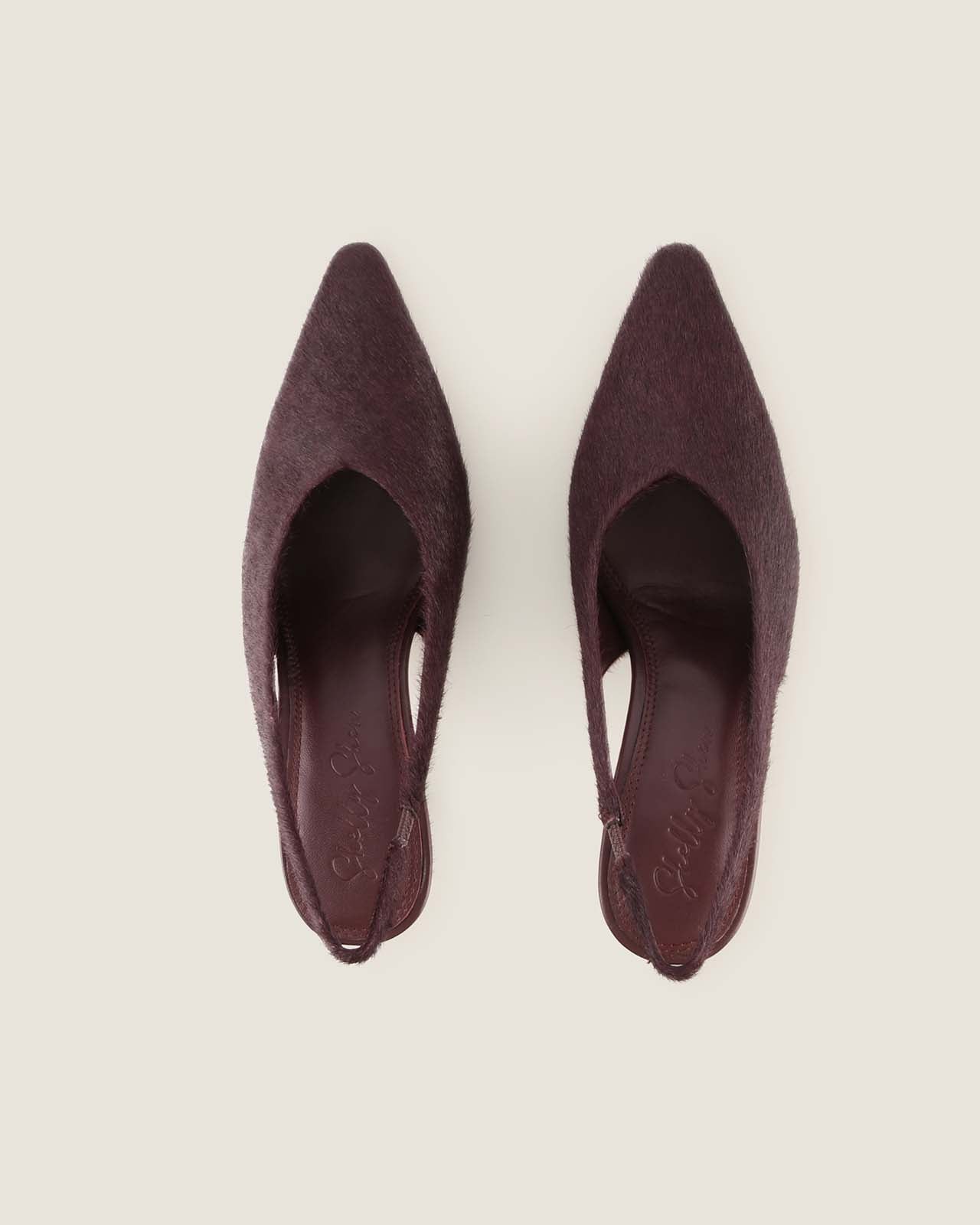 Pair of maroon pointed-toe shoes on a light beige background